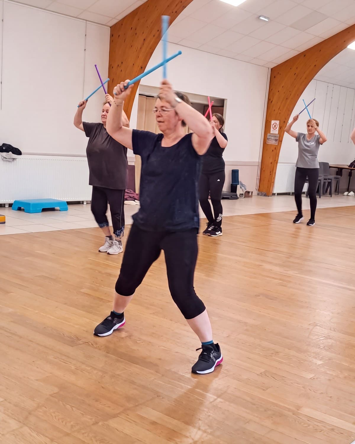 Cours de fitness du club, bras levés et bâtons lestés, dans la salle communale.
