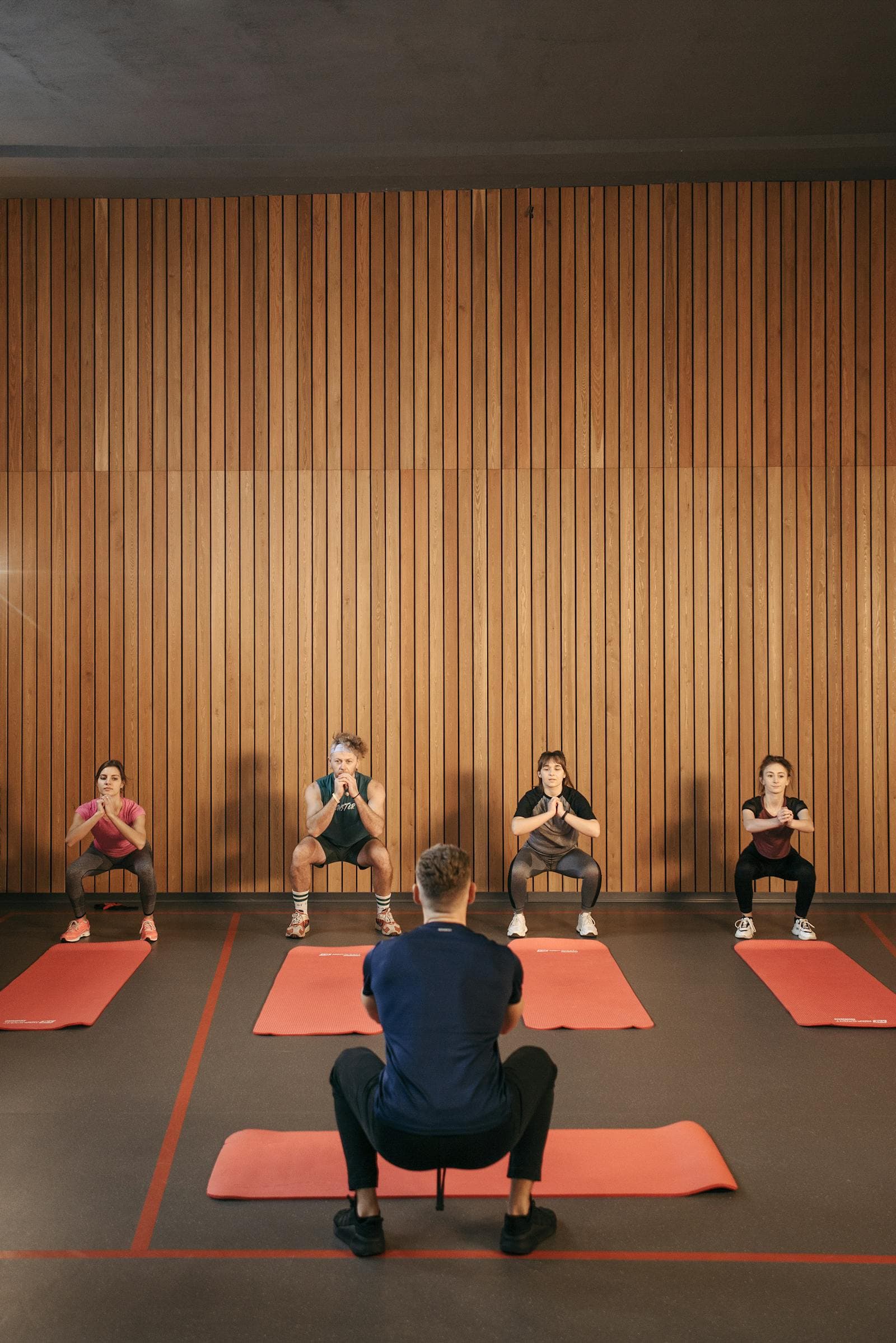 Cours collectif en salle, série de squats face à l'éducatrice sportive.