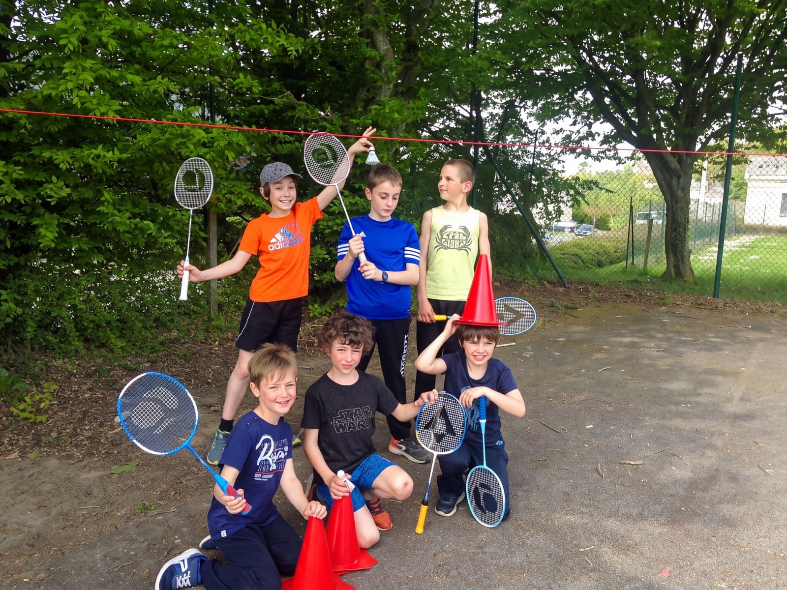 Sept enfants posent dehors avec leurs raquettes de badminton, filet tendu derrière eux.