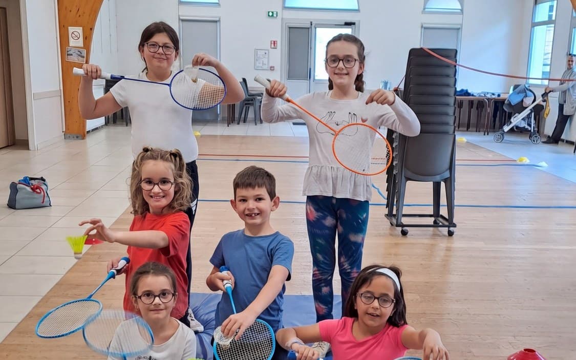 Six enfants posent avec leurs raquettes de badminton dans la salle du club.