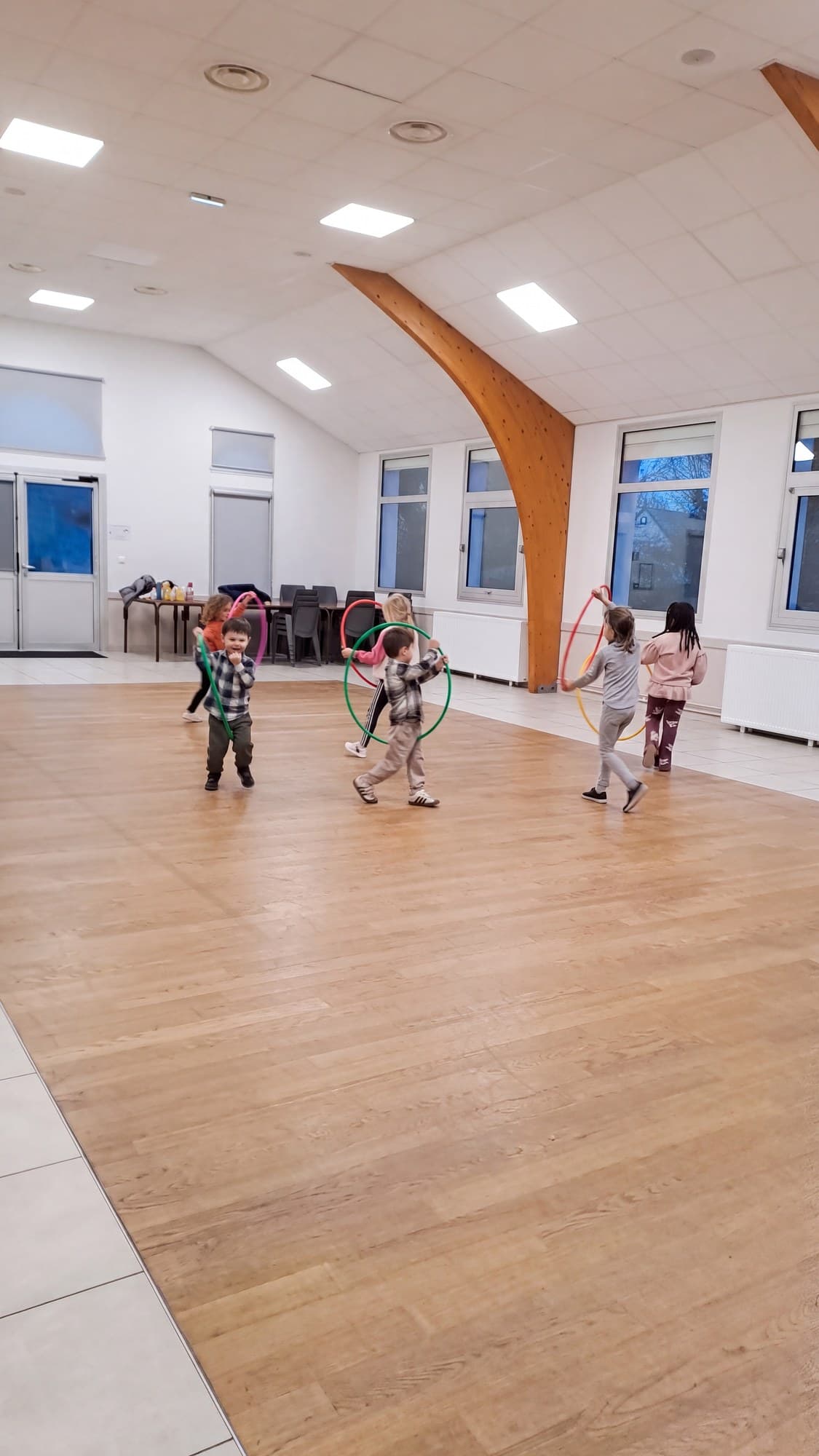 Cinq enfants font tourner des cerceaux colorés dans la salle du club.