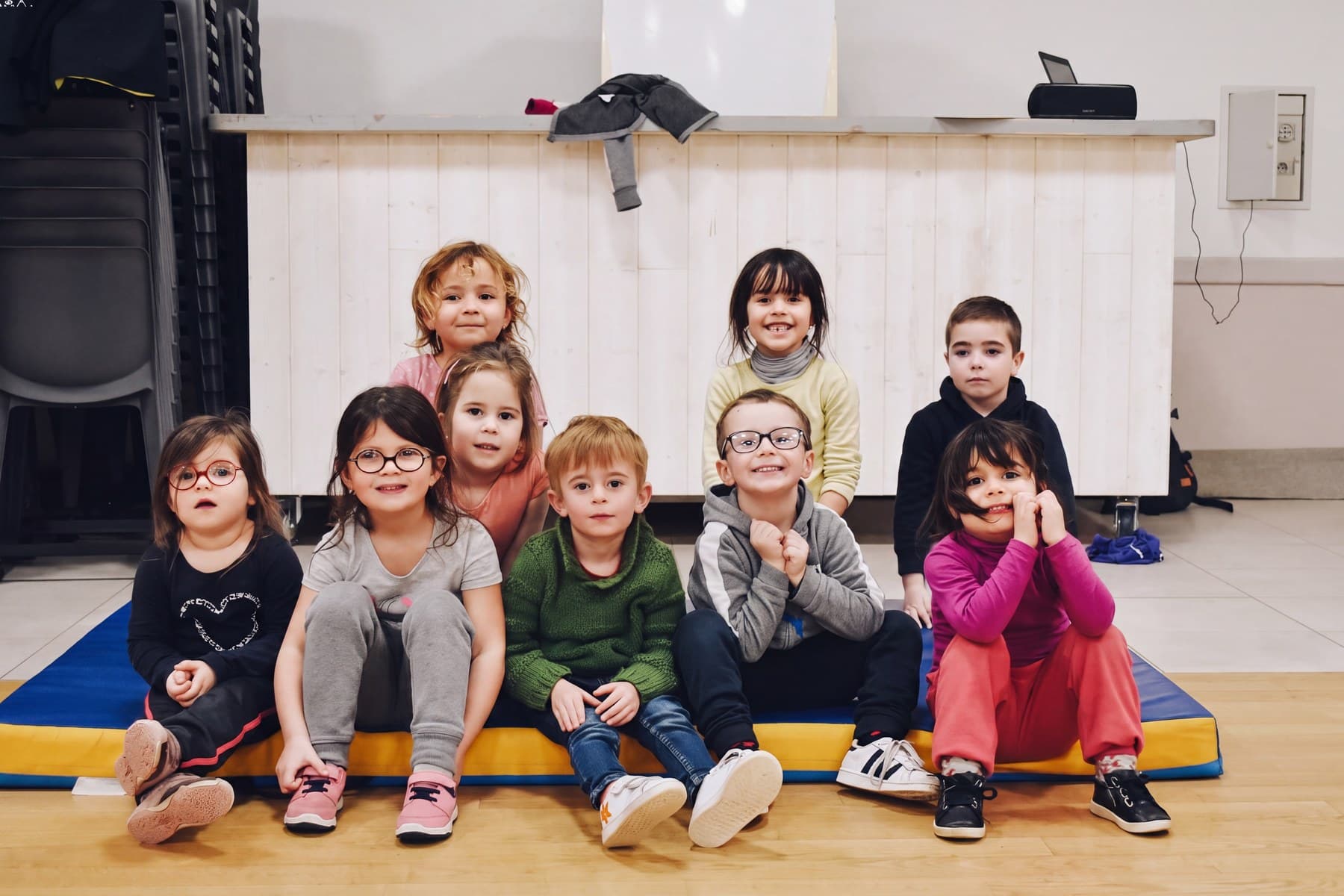 Le groupe de l’éveil enfants assis sur les tapis colorés, tous tournés vers l’objectif.