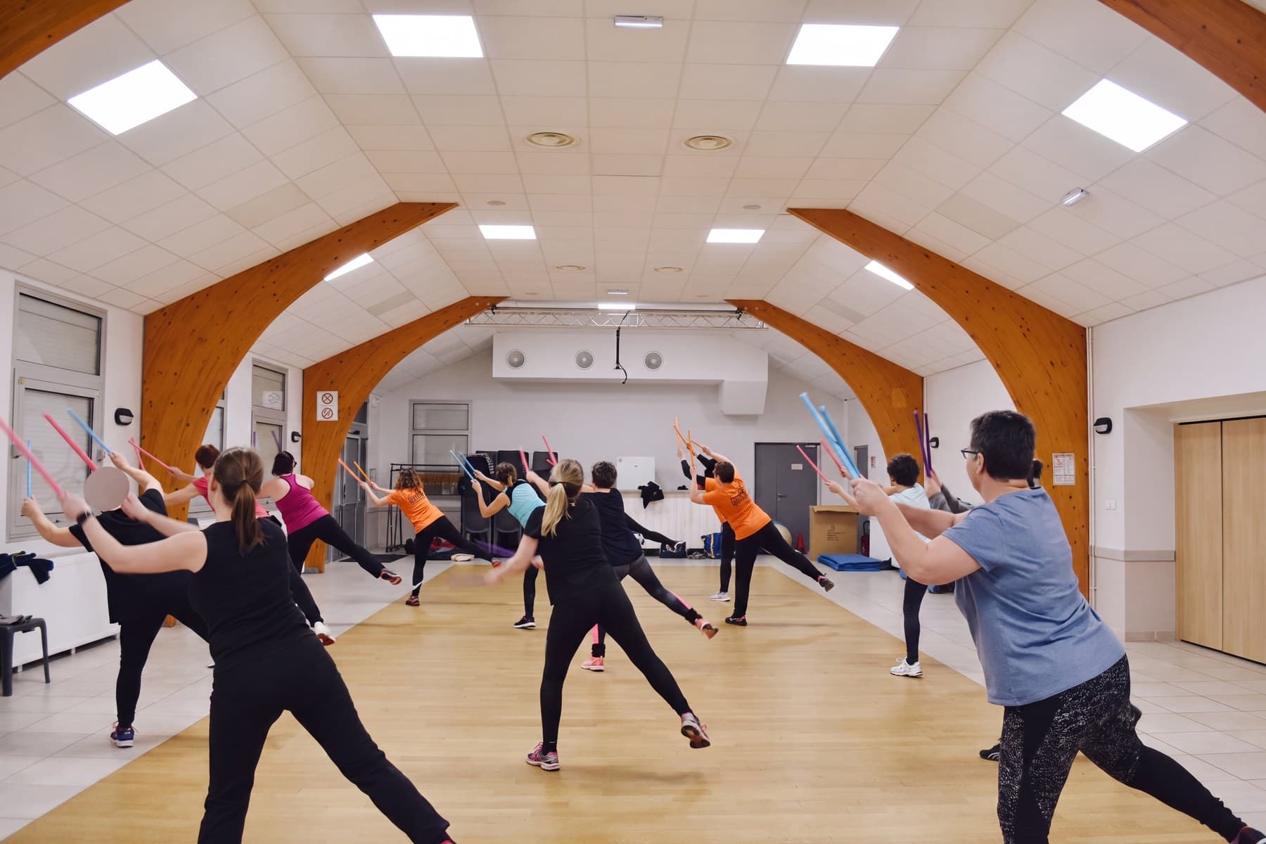 Le cours de fitness en fente large, bâtons tendus, l’éducatrice face au groupe.
