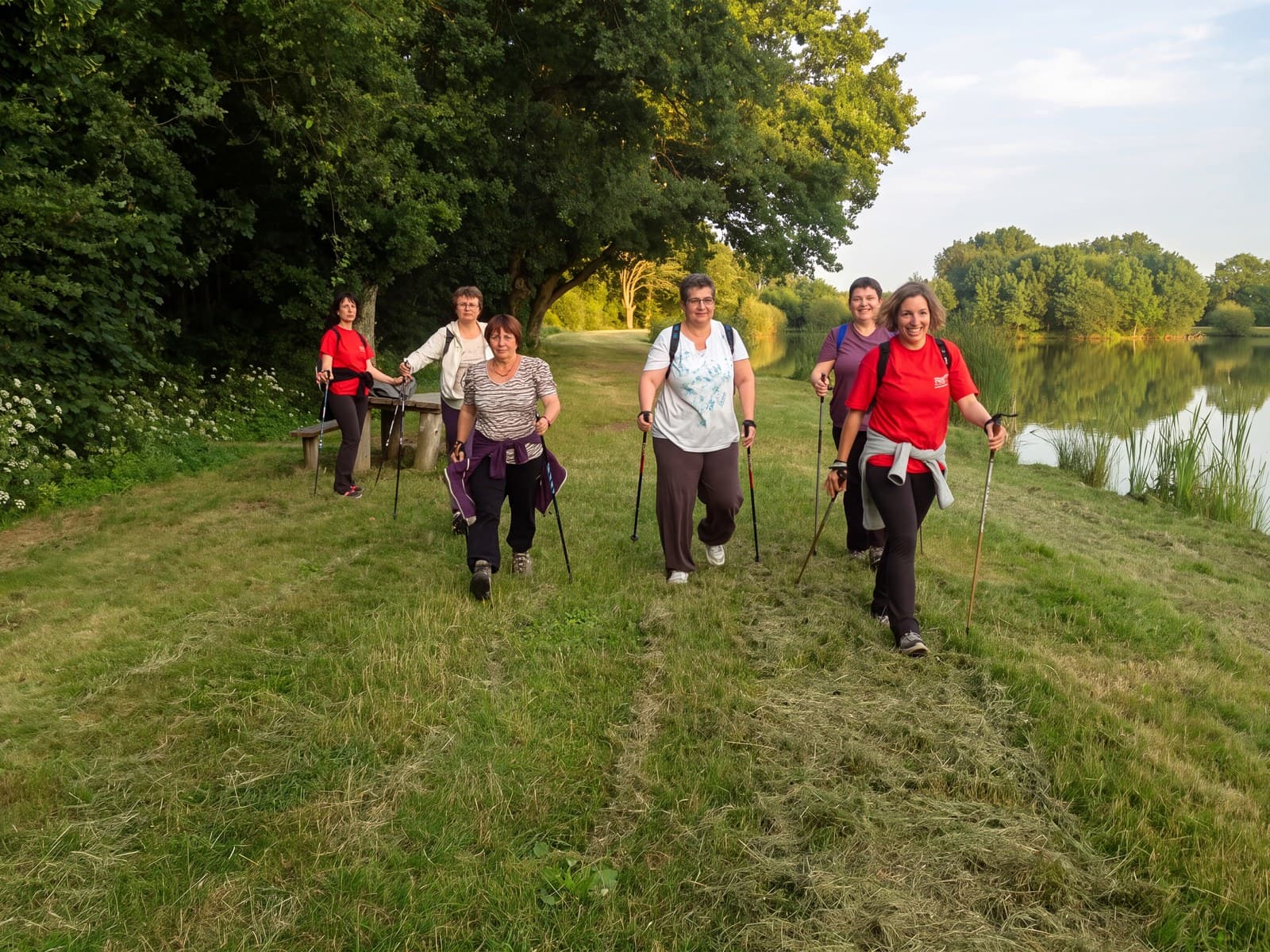 Le groupe de marche nordique avance vers l’objectif sur un chemin d’herbe, un étang à droite.