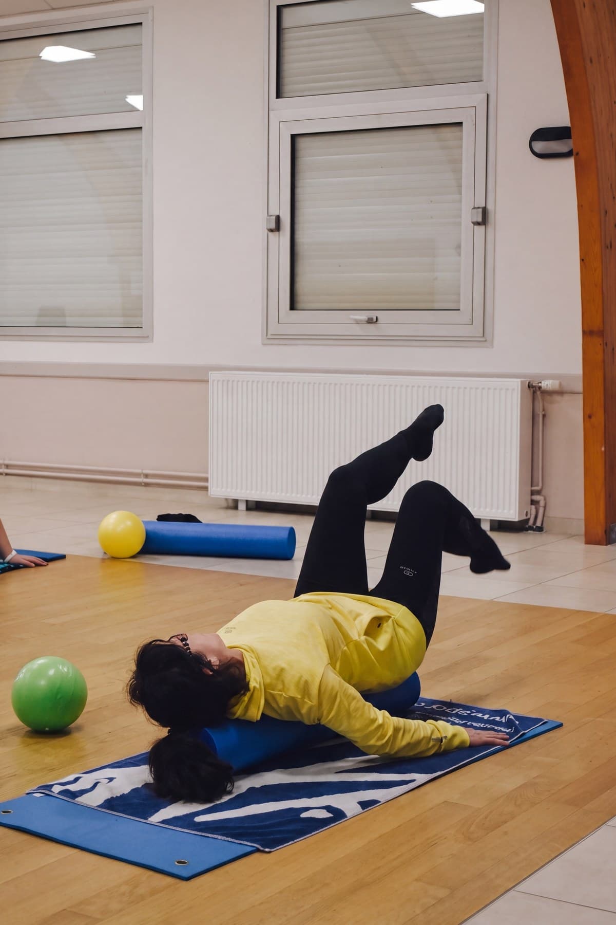 Une adhérente en position de pont sur un tapis, jambes levées, ballons posés à côté.