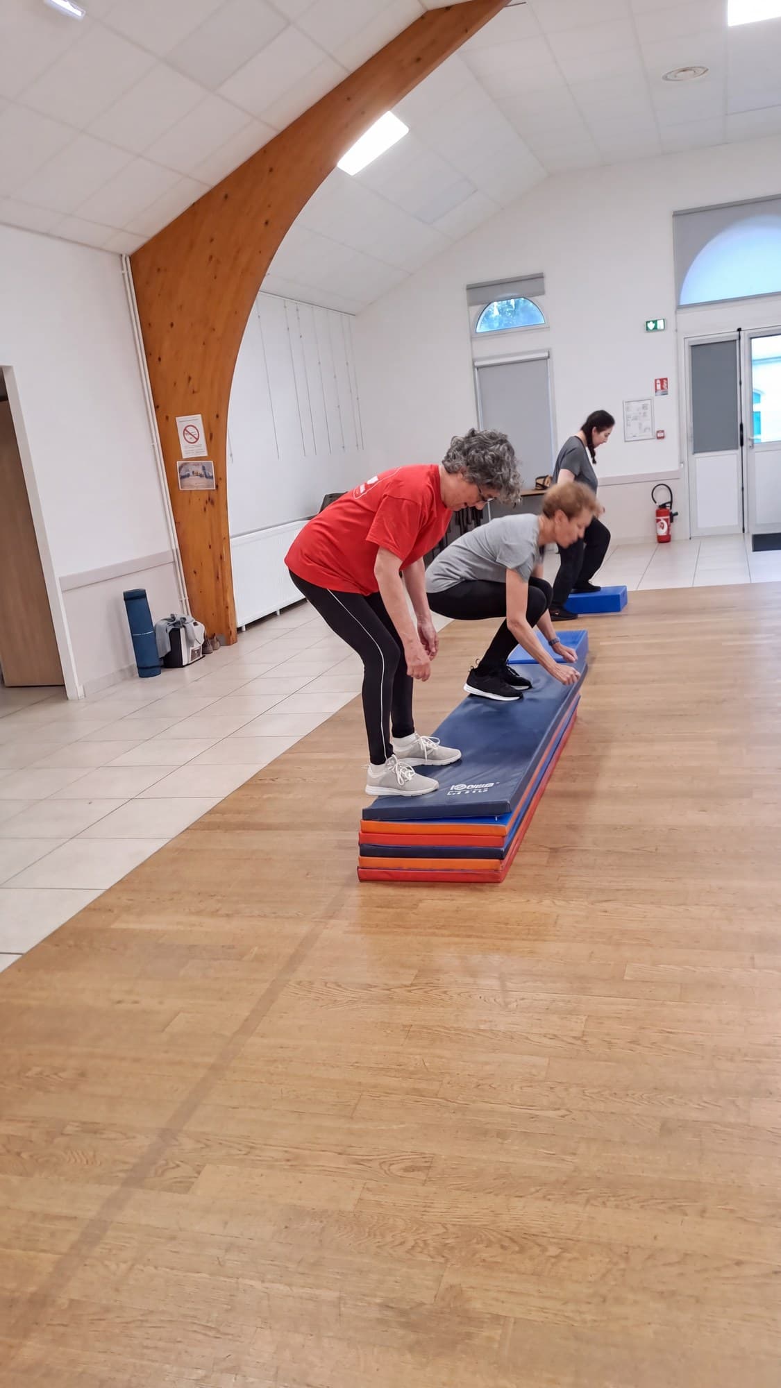 Trois adhérentes séniors montent sur un empilement de tapis, l’une derrière l’autre.