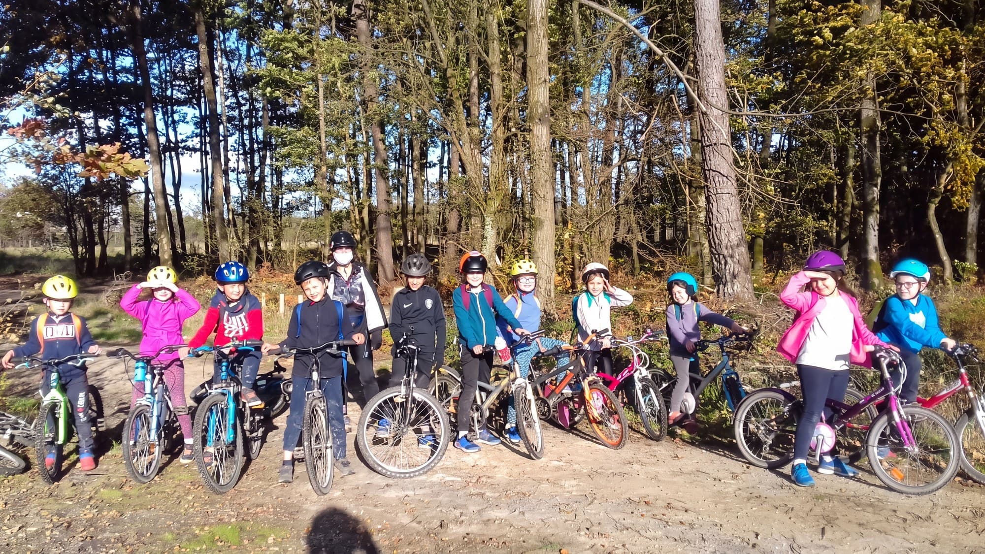 Une douzaine d'enfants casqués alignés avec leurs vélos sur un chemin forestier.